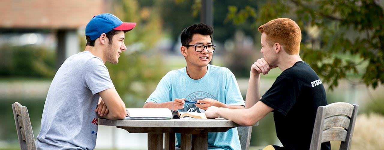 Three male students do homework at a patio table